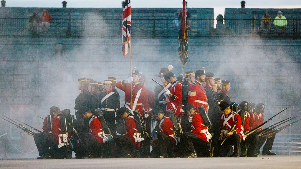 Soldaten der Fort Henry Guard in historischen roten Uniformen führen in der Abenddämmerung in Kingston, umgeben von Rauch, eine zeremonielle Übung durch.