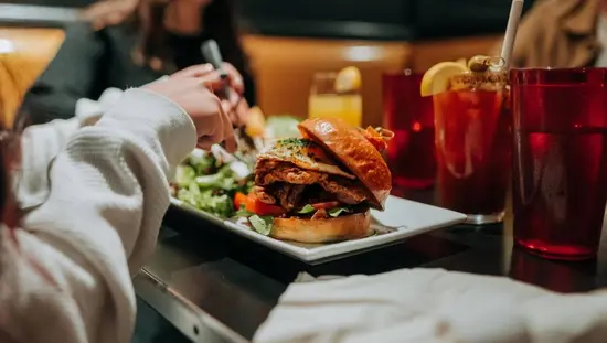 Una jugosa hamburguesa con muchos ingredientes adicionales, servida con ensalada y una bebida afrutada.