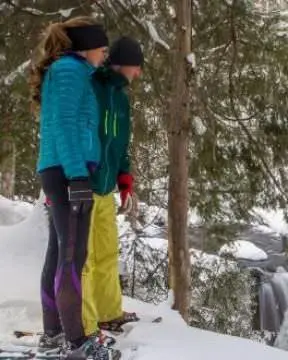 A couple snow shoeing and looking down at the ground