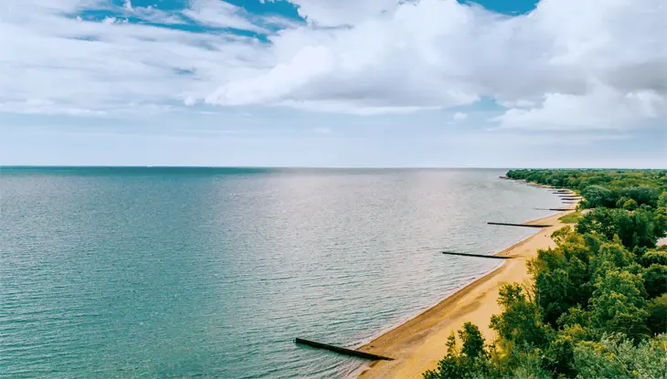Una vista aérea de una hermosa agua azul verdosa, una larga playa de arena y exuberantes árboles verdes en Canatara Park Beach, Sarnia.