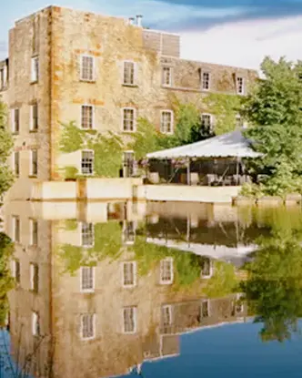 Edificio patrimonial de piedra de Millcroft Inn & Spa reflejado en un estanque tranquilo, rodeado de exuberantes árboles verdes.