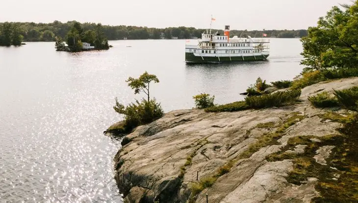 Ein historisches Passagierdampfschiff fährt an der felsigen Küste und bewaldeten Inseln in Muskoka vorbei.